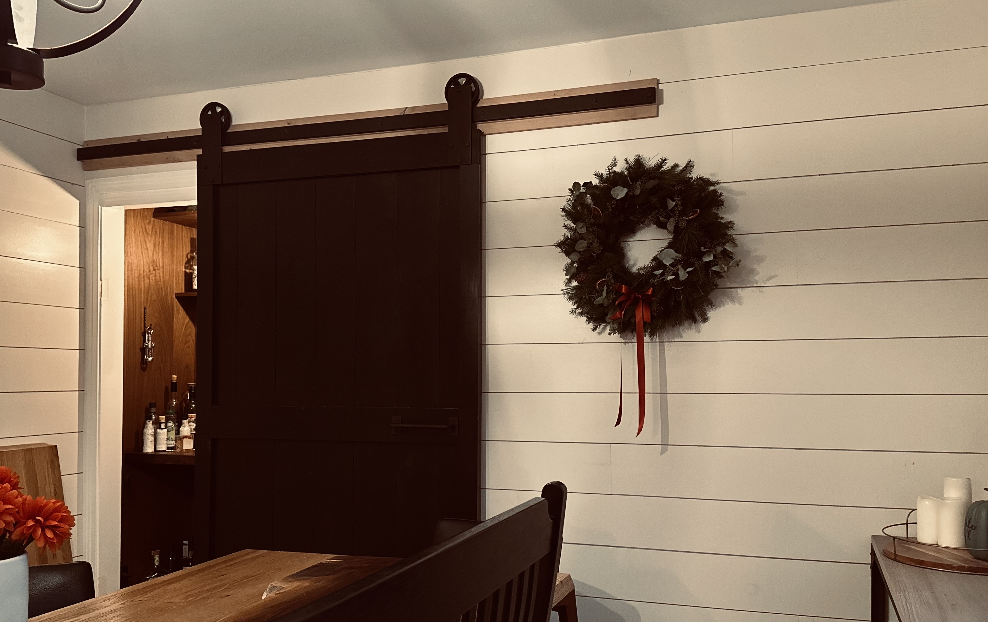 Sliding dark wood door partially open to reveal a concealed bourbon closet in a dining room